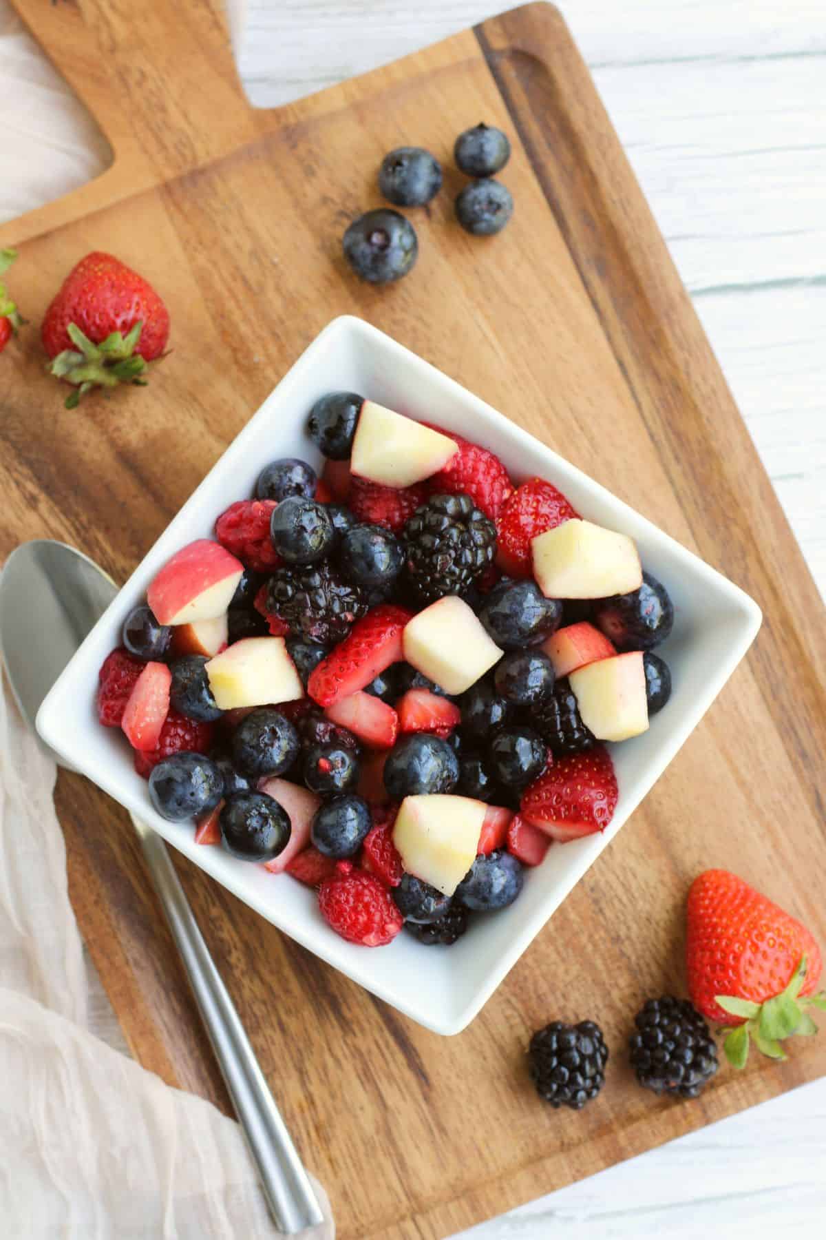 An overhead of fresh summer fruit in a square bowl with fresh fruit on the cutting board around the bowl.