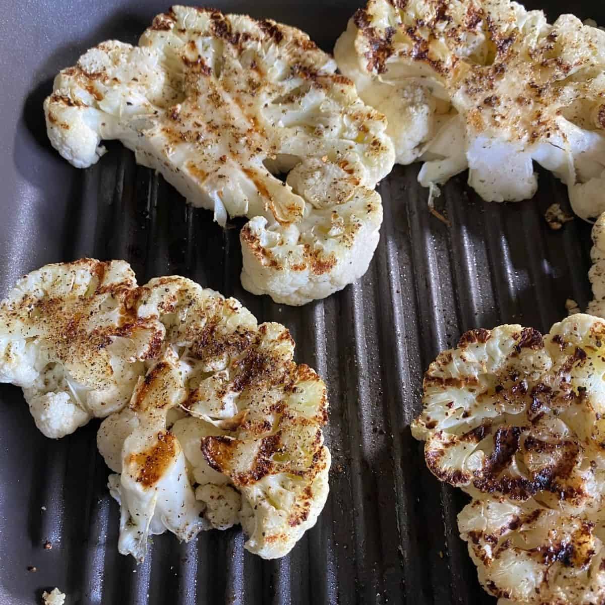 A grill pan with cauliflower steaks in the pan. 