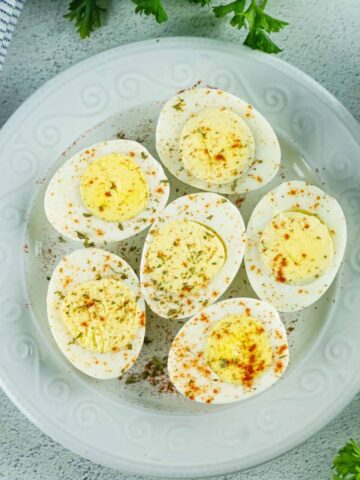 An overhead view of hard boiled eggs on a grey plate sliced in half with paprika sprinkled on the eggs.
