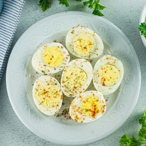 An overhead view of hard boiled eggs on a grey plate sliced in half with paprika sprinkled on the eggs.