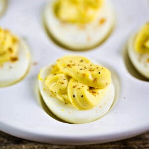 A white egg holder plate with cooked egg whites topped with a creamy yellow filling topped with cracked black pepper and paprika.