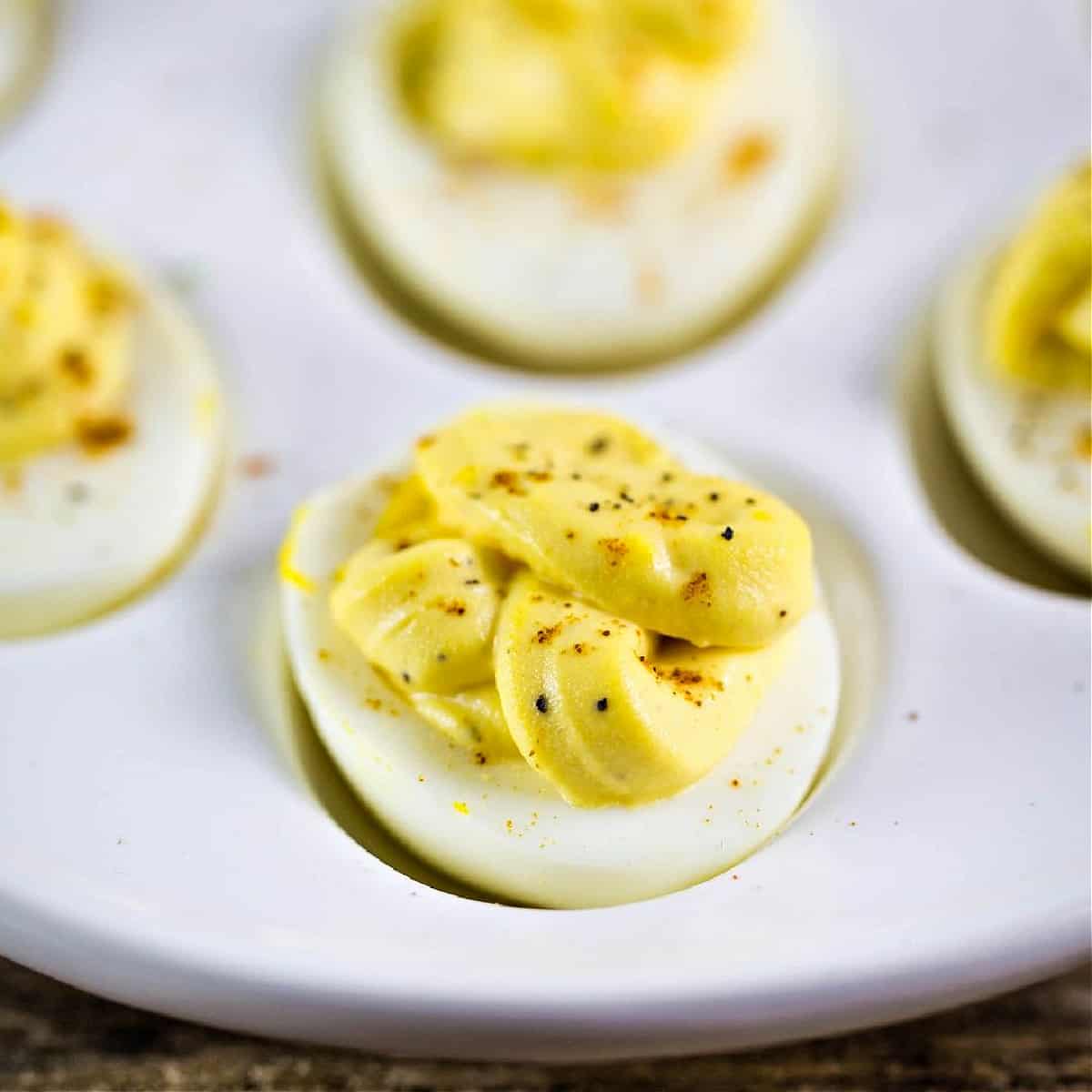 A white egg holder plate with cooked egg whites topped with a creamy yellow filling topped with cracked black pepper and paprika.