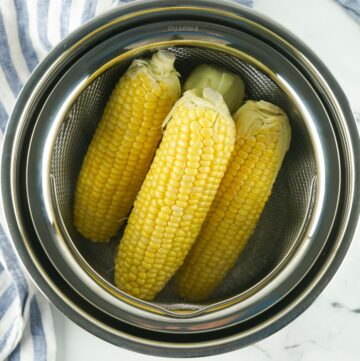 An Instant pot opened with a trivet inside topped with 3 ears of corn.