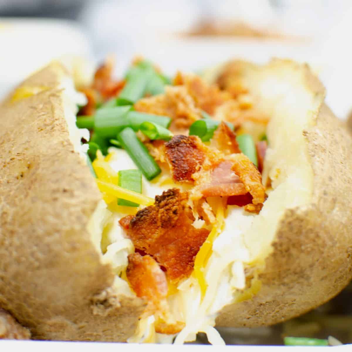 A sliced baked potato topped with chopped bacon, shredded cheese, and green onions. 