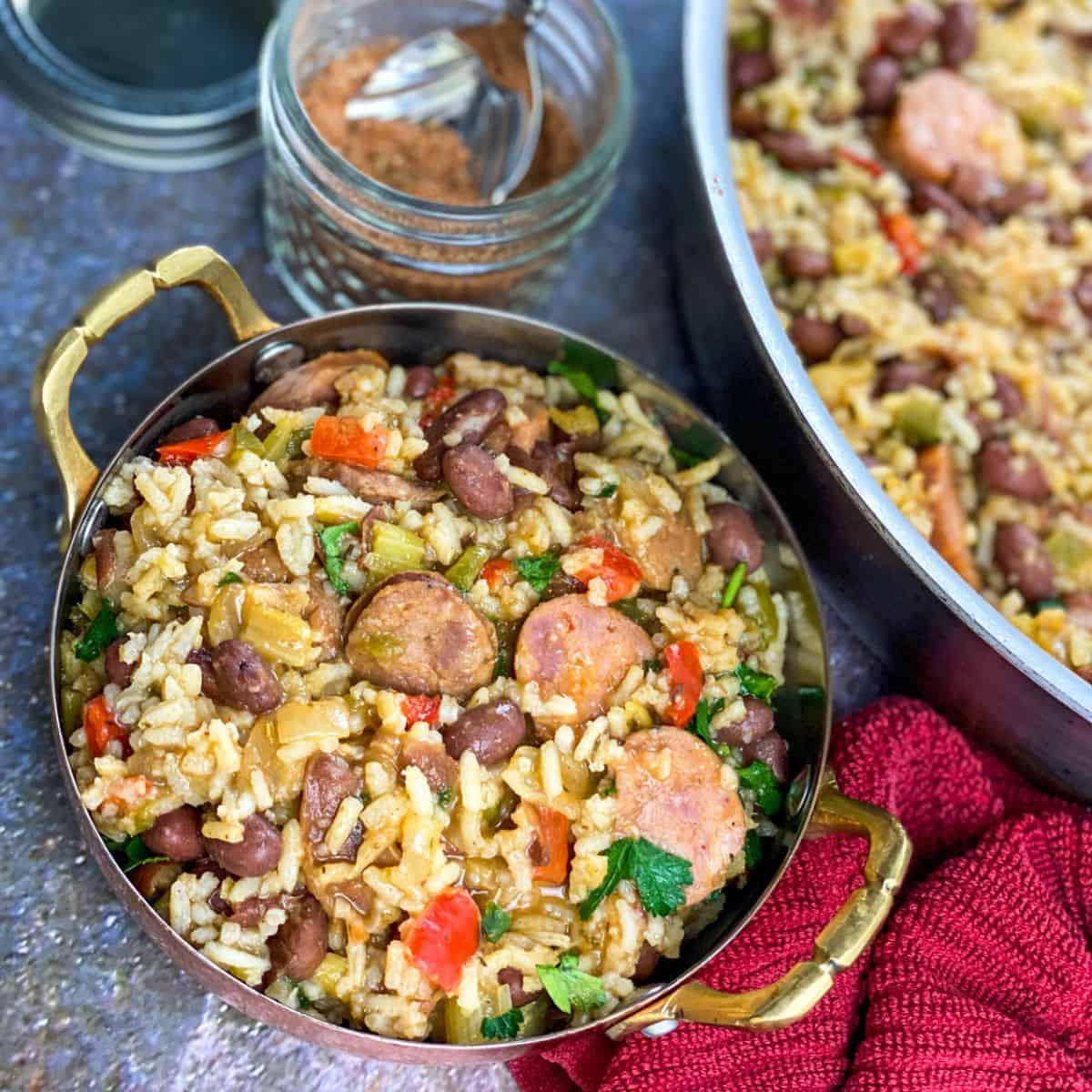 A large gold handled skillet filled with rice, sliced smoked sausage, beans, and peppers.