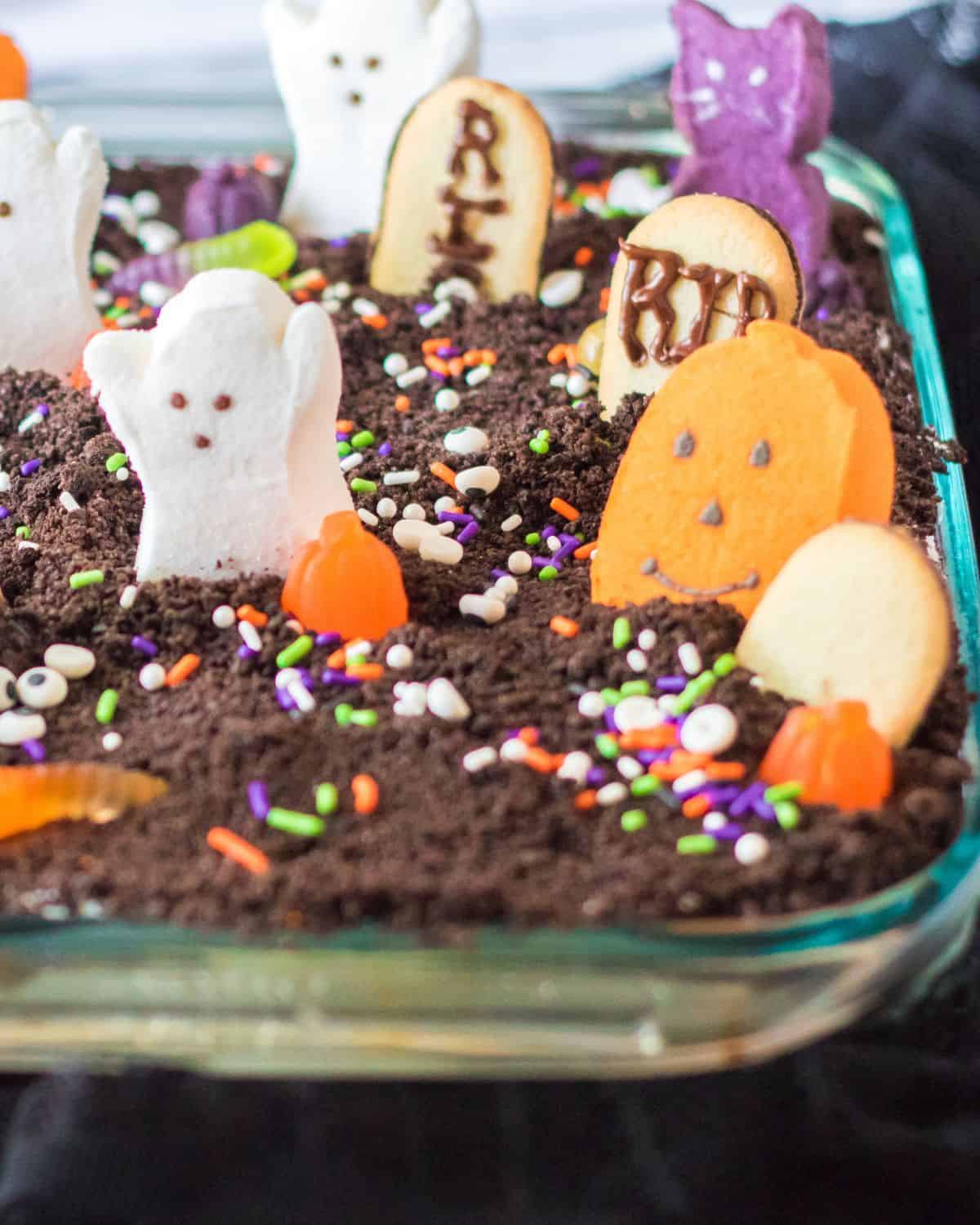 A Halloween cake decorated with marshmallow ghosts, pumpkins, and cemetery cookies