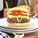 A stack of white plates with a cheeseburger with lettuce and tomato in a bun on the stack of plates.