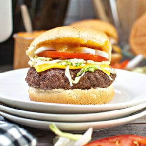 A stack of white plates with a cheeseburger with lettuce and tomato in a bun on the stack of plates.