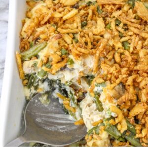 A white casserole dish with green beans and chicken in a cream sauce topped with fried onions.