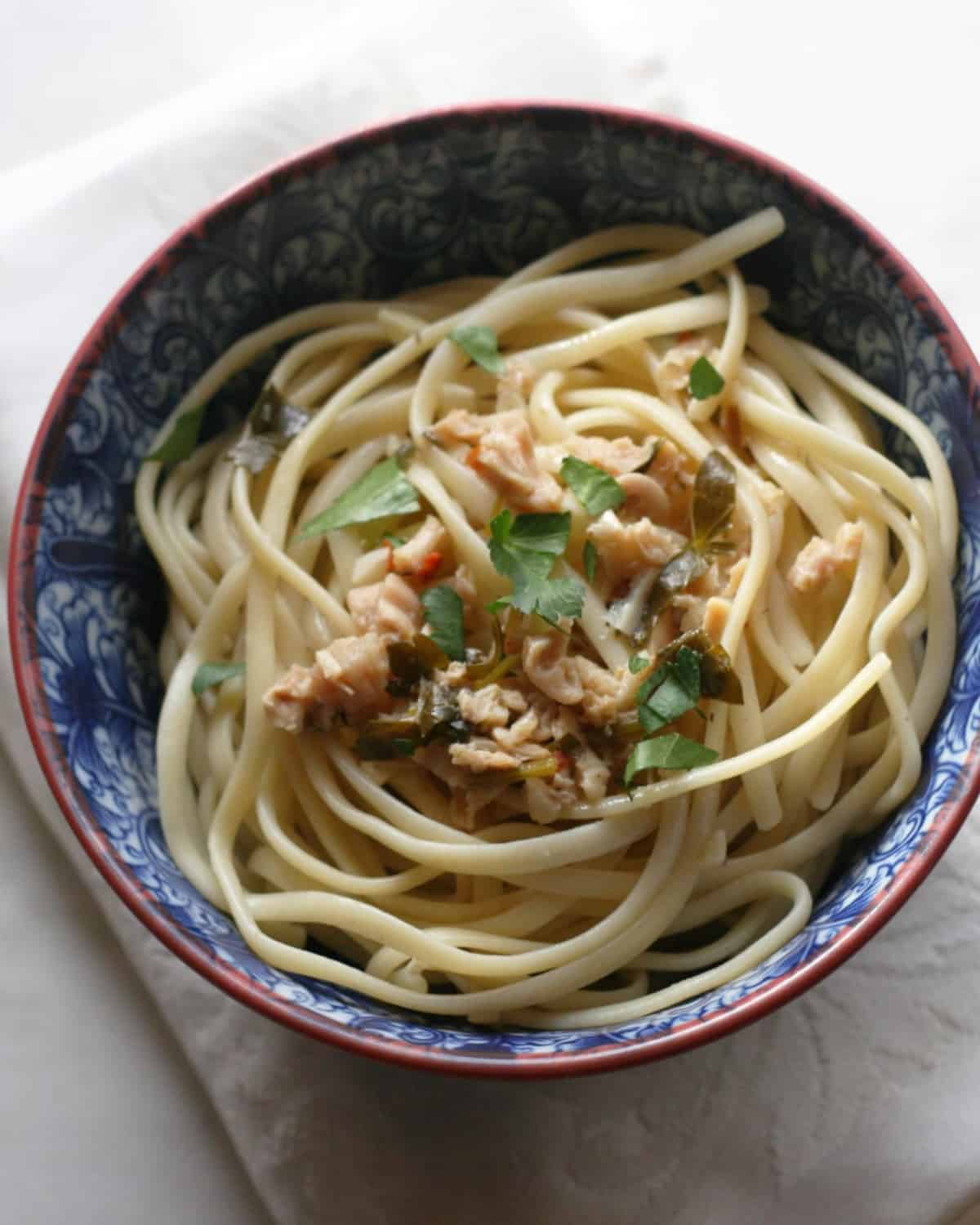 A blue flower bowl with linguine, chopped clams, and chopped herbs.