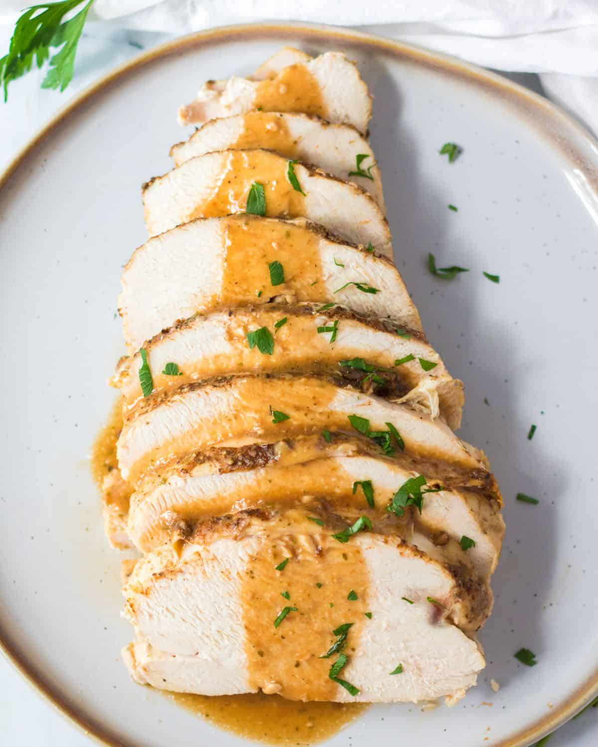Sliced Turkey meat on a platter drizzled with gravy and chopped parsley.