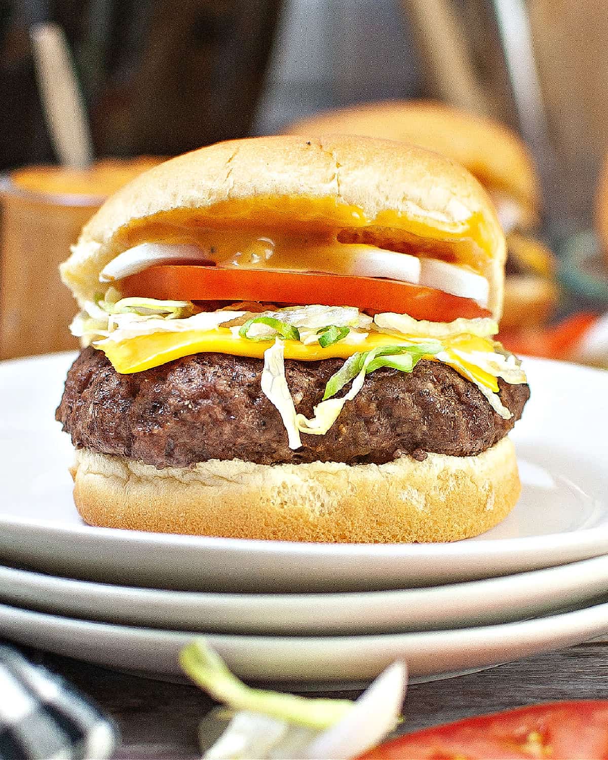 A hamburger with cheese, lettuce, and tomatoes on a hamburger bun on white plate.