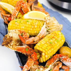 A crab boil set on a blue linen with corn, crab legs and potatoes.