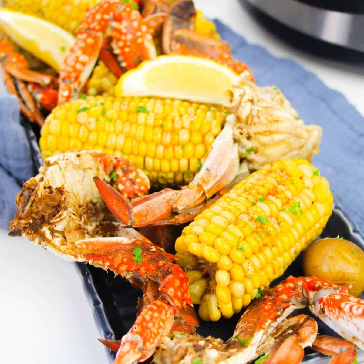 A crab boil set on a blue linen with corn, crab legs and potatoes.