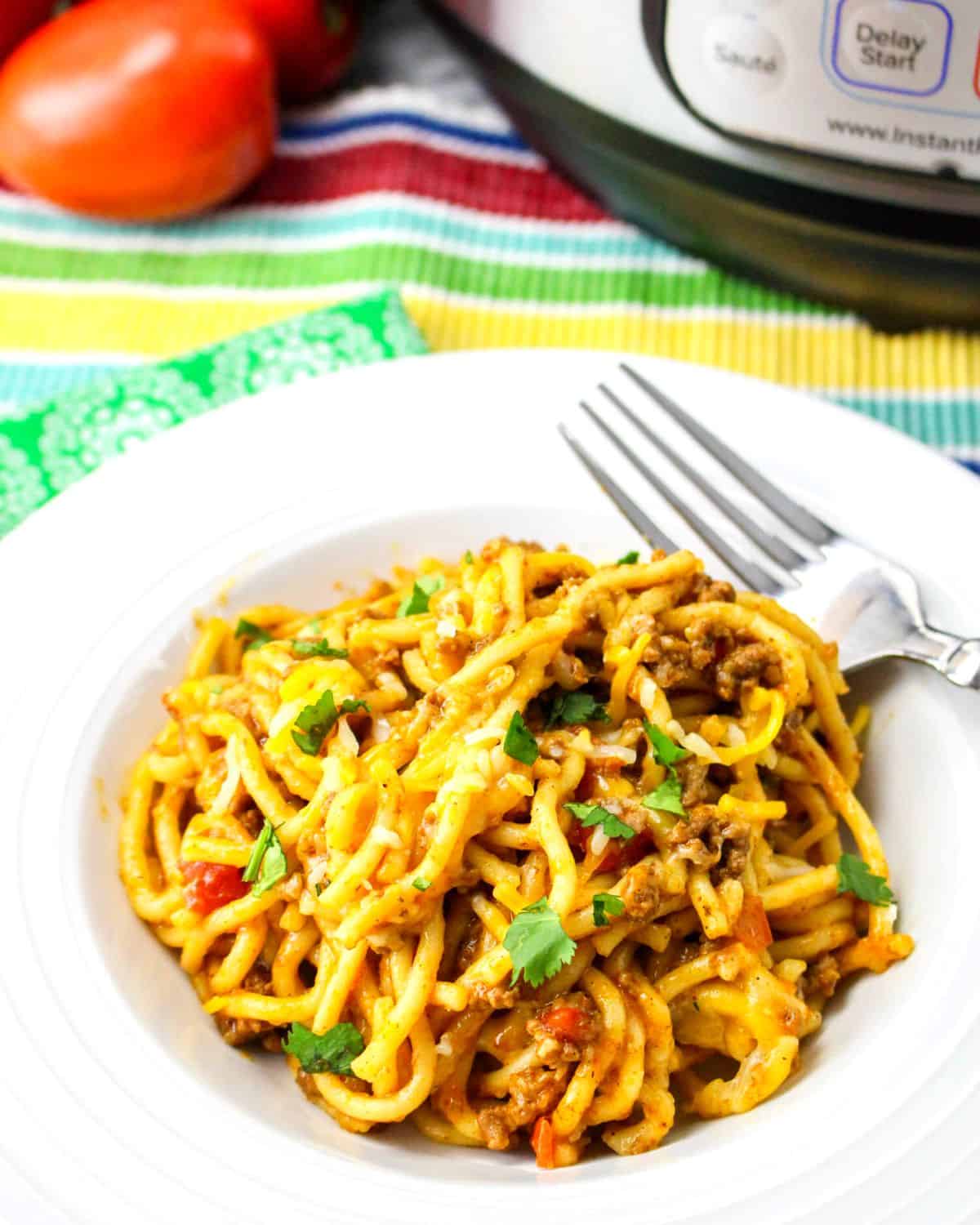 A white bowl of spaghetti with taco seasonings in front of an Instant Pot.