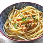 A blue and white bowl with pasta and diced clams and fresh chopped herbs.