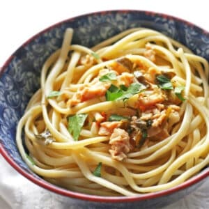 A blue and white bowl with pasta and diced clams and fresh chopped herbs.