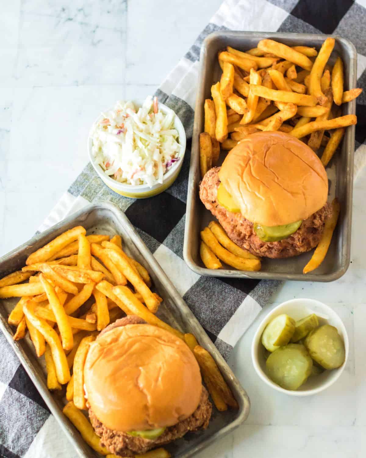 An overhead view of fried chicken sandwiches on brioche buns with fries and pickles on the side. 