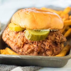 A closeup of a chicken sandwich that is fried with the seasonings of a popeyes sandwich on a brioche bun with a pickle.