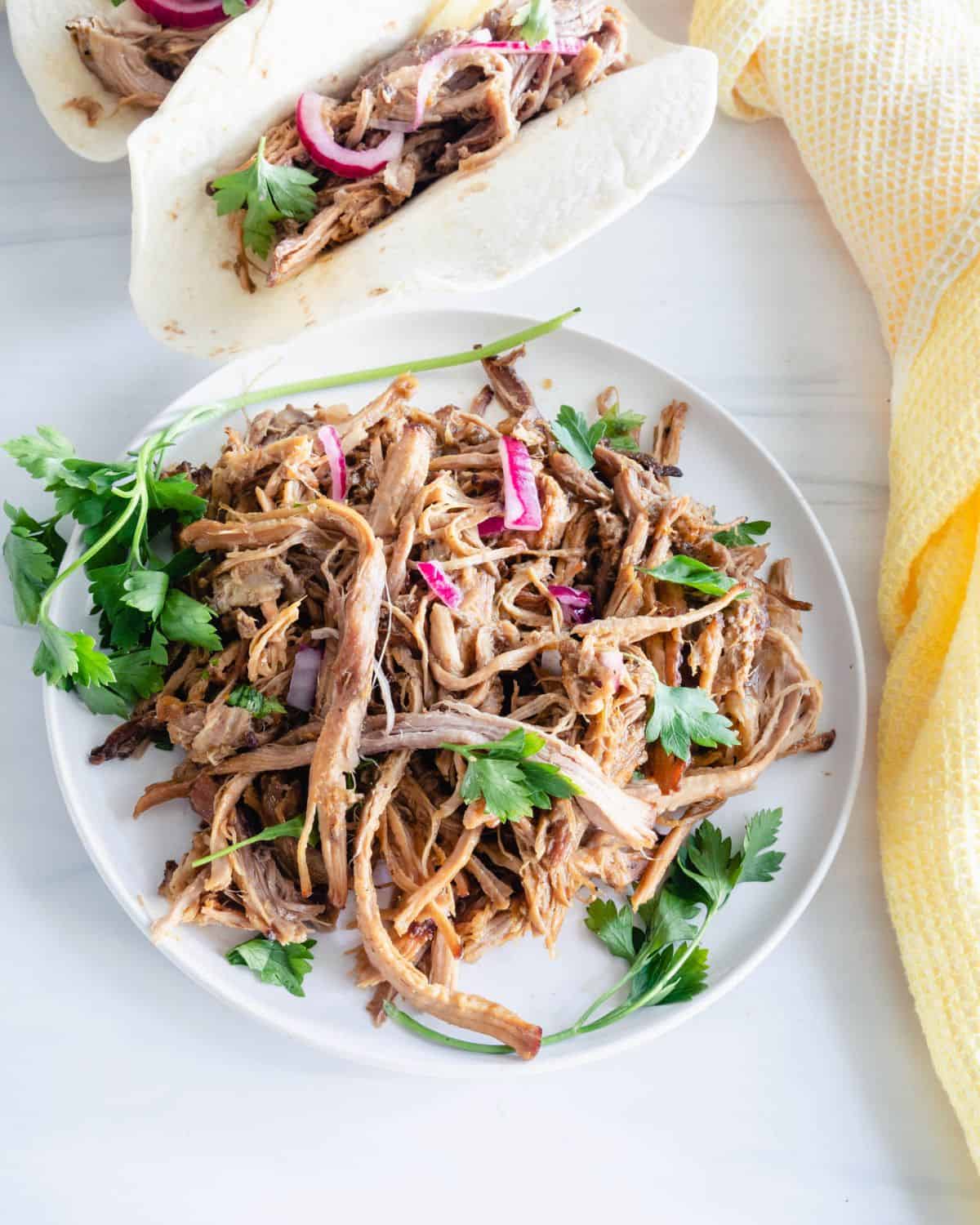 Pork carnitas on a white plate with shredded pork, chopped cilantro, red onions on it. 