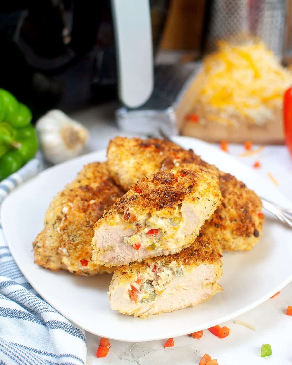 Chicken breasts stacked on a white platter, sliced with a center of cheese and diced peppers.