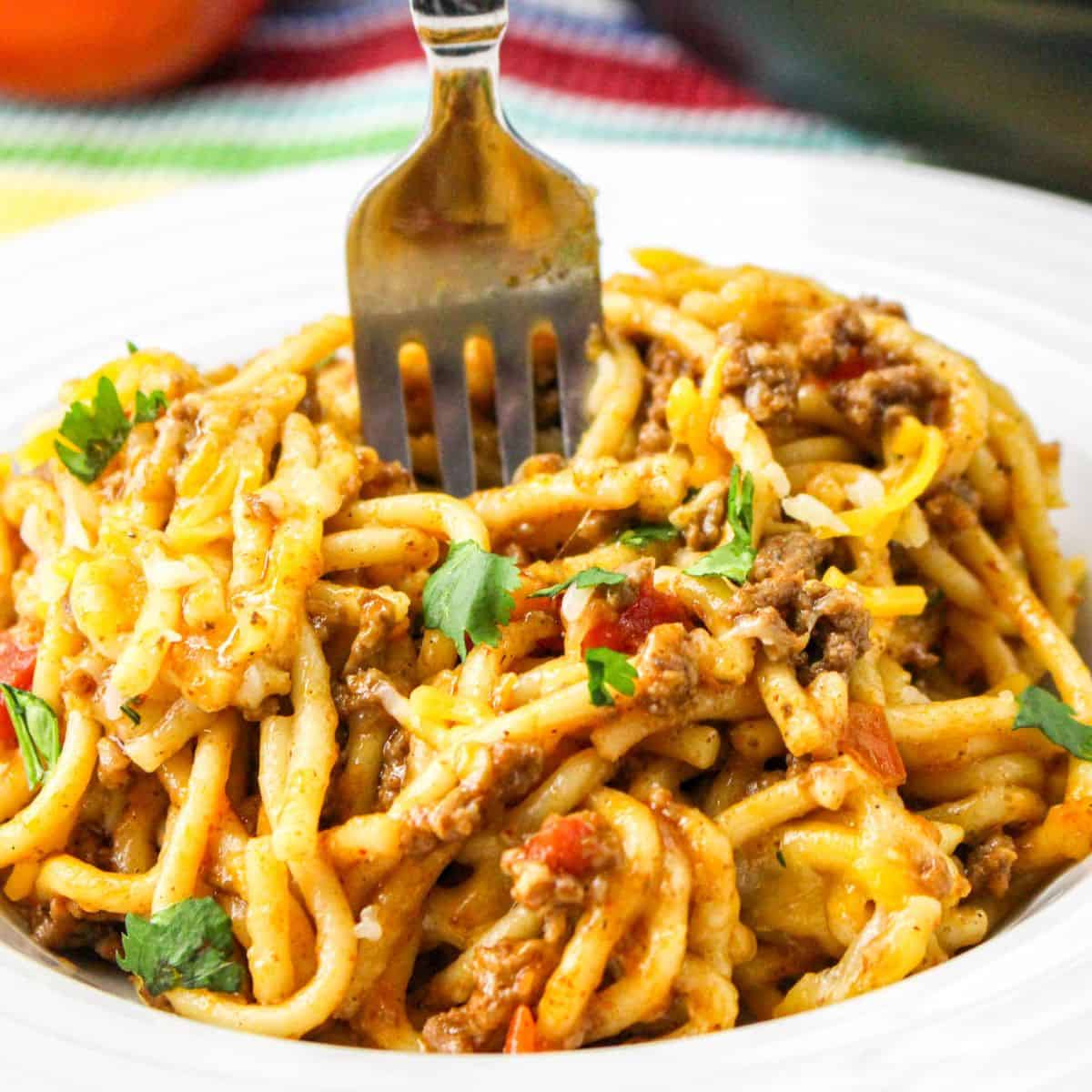 A white bowl of spaghetti with taco seasoning and a fork in the center of the bowl. 