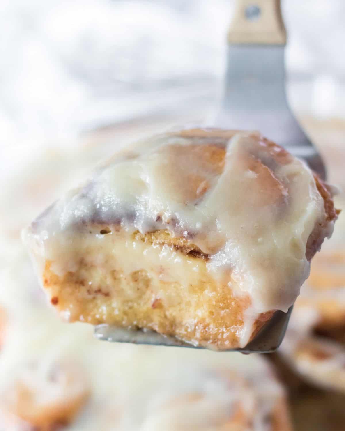 A cinnamon roll on a spatula being picked up. 