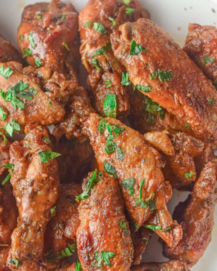 Chicken wings on a white plate with a red sauce and sprinkled with fresh parsley.