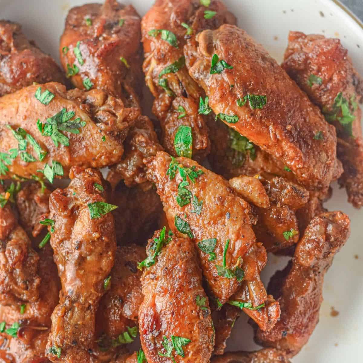 Chicken wings on a white plate with a red sauce and sprinkled with fresh parsley.