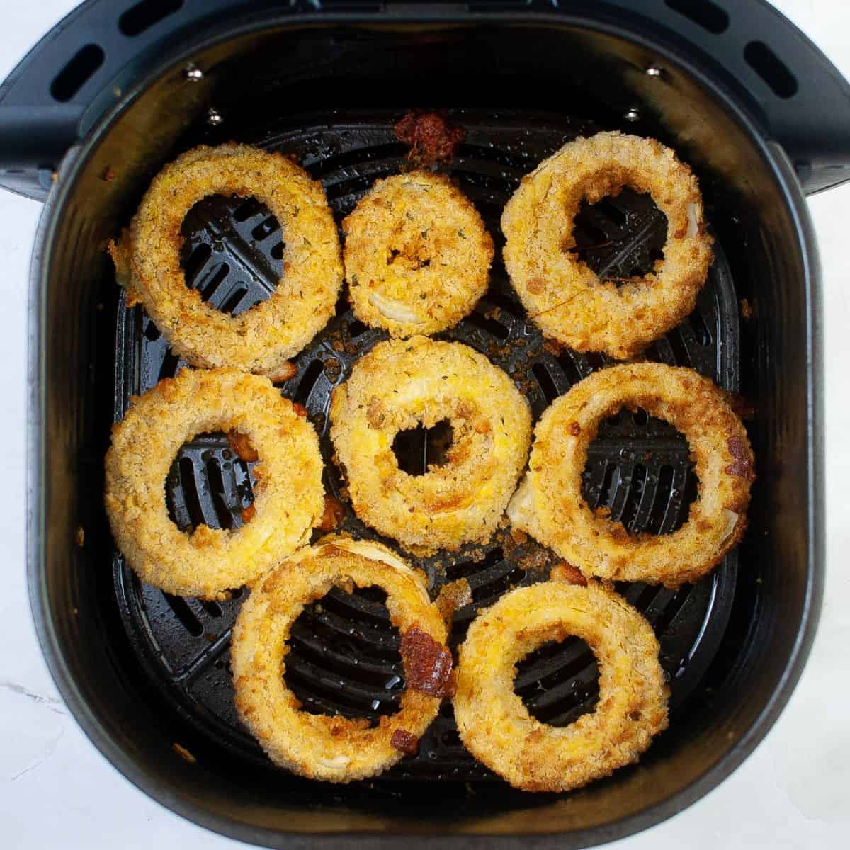 Air fryer basket with cooked onion rings coated with panko bread crumbs.