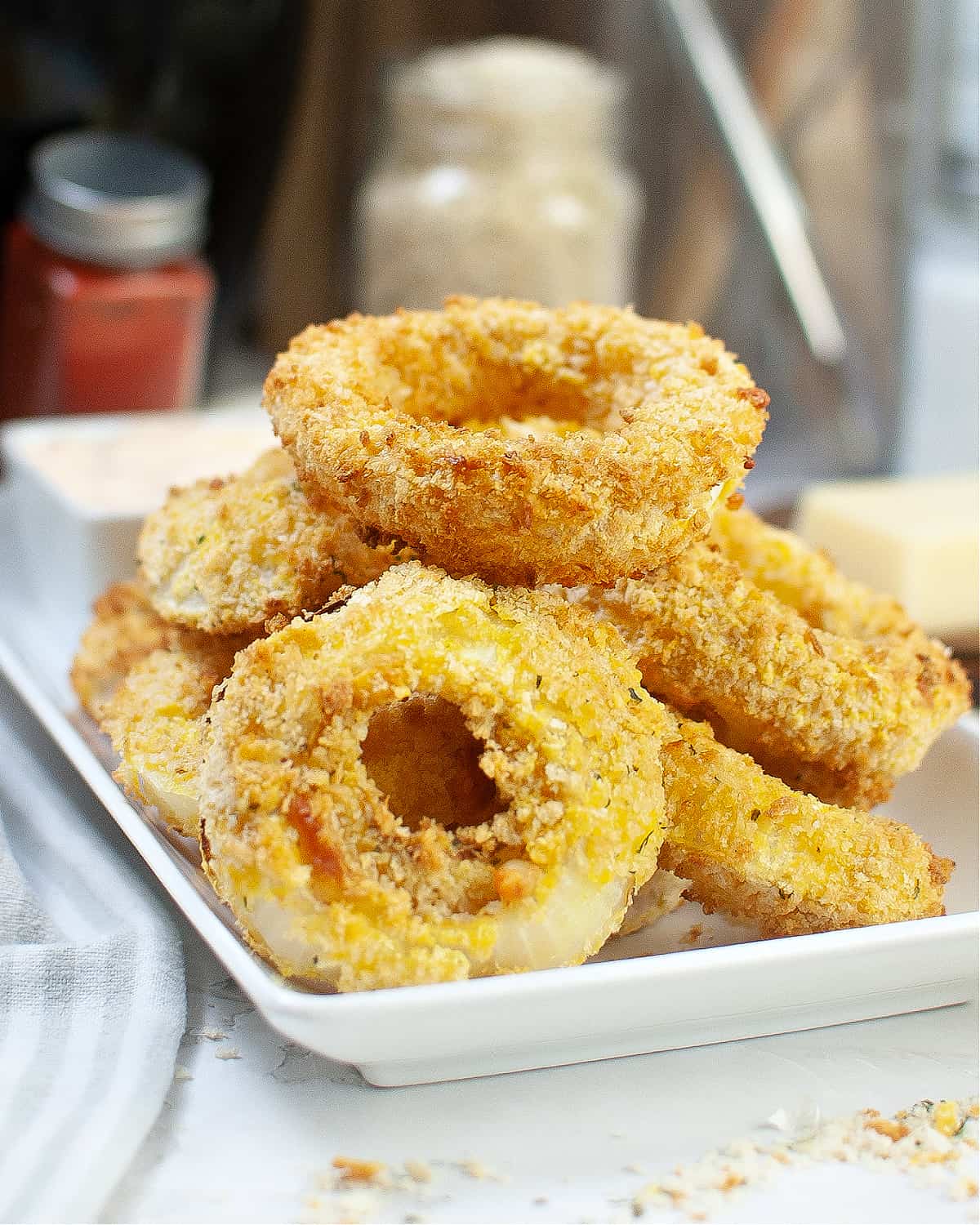 A white plate with onion rings that have been air fried and stacked on the plate.