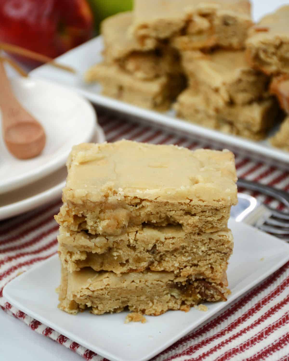 A white plate on a red and white striped linen with a stack of blondies with chopped apples on it.