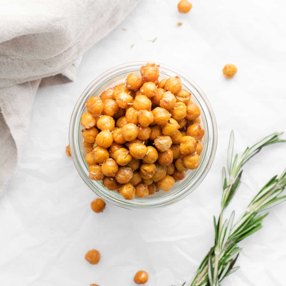 An ovehead view of chick peas in a glass bowl with rosemary herb to the side of the bowl.