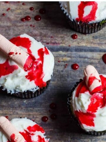 Edible blood topped cupcakes with fingers in the cupcake icing.