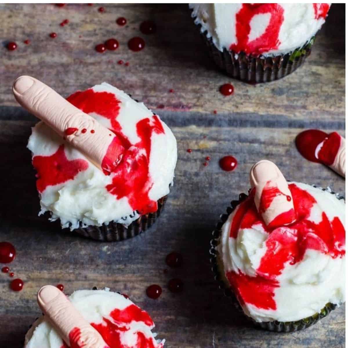 Edible blood topped cupcakes with fingers in the cupcake icing.