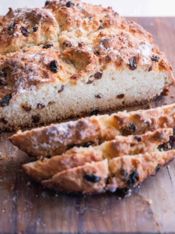 A round bread with raisins, sliced on a cutting board.