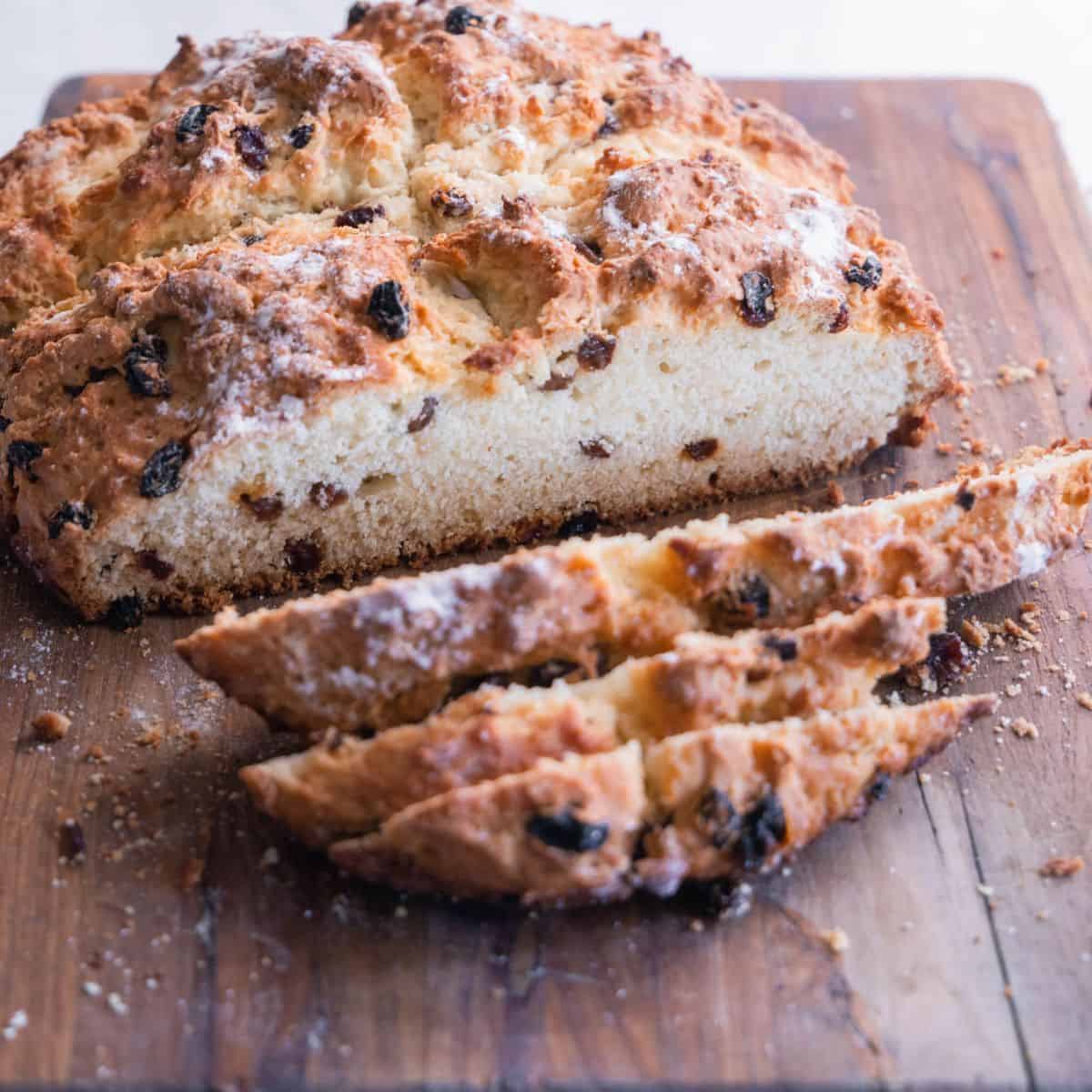 A round bread with raisins, sliced on a cutting board.