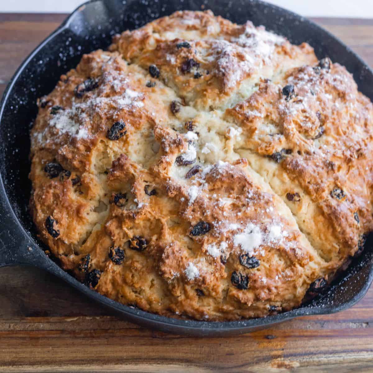 A cast iron pan with a baked bread in it. The bread has an indent in it shaped like a cross. 