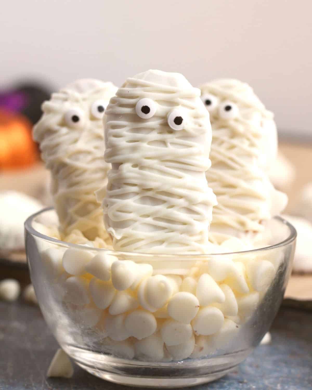 Mummy cookies on a bed of marshmallows in a glass cup.