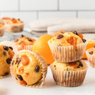 Orange muffins with fresh oranges and chocolate chips staggered on a white plate.