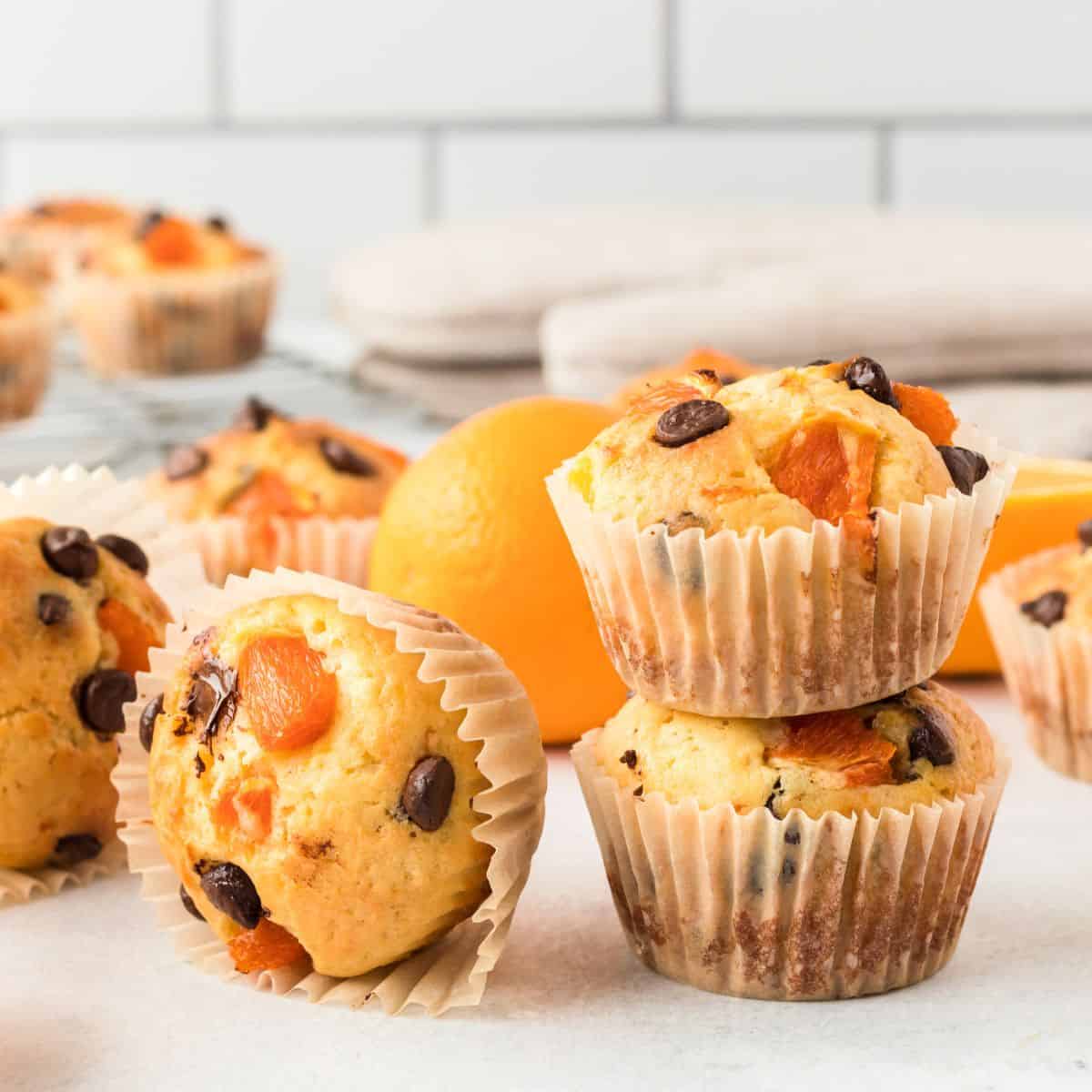 Orange muffins with fresh oranges and chocolate chips staggered on a white plate.