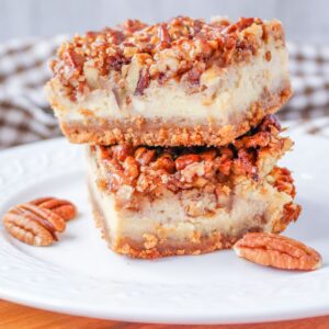 Two pecan pie cheesecake bars stacked on a white plate.