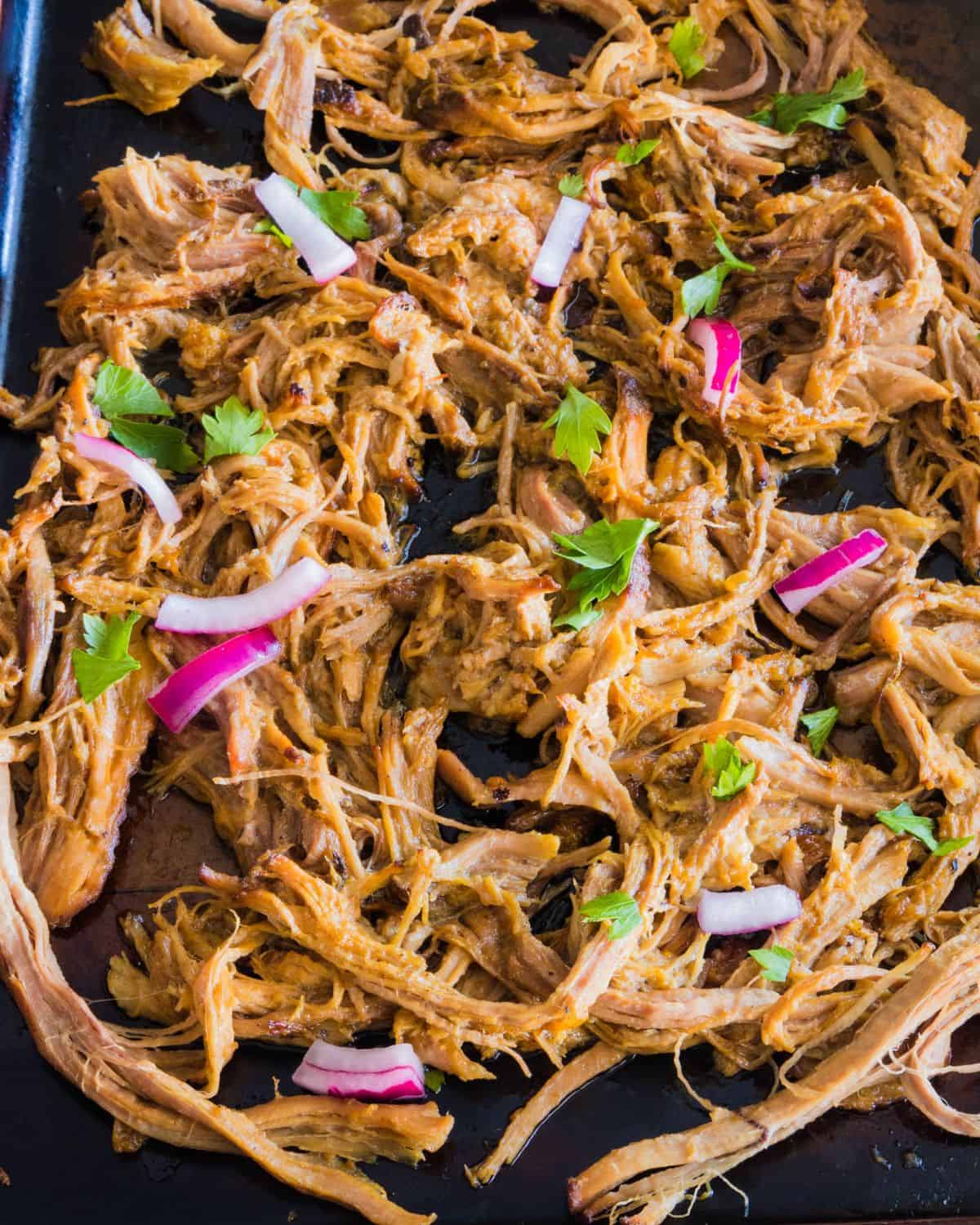 A baking pan with shredded cooked pork to make pork carnitas