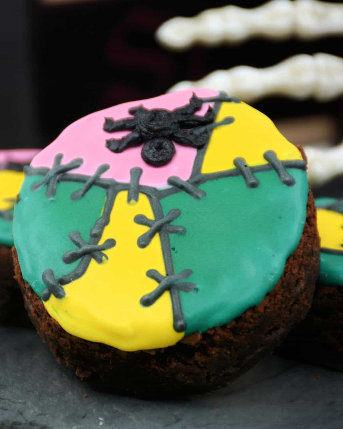 A brownie with green, pink, and yellow coloring and black icing depicting stitches for Halloween brownies. 