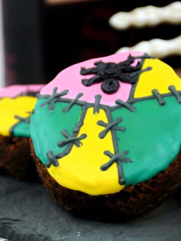 A round brownie decorated with green, yellow, and pink icing with a spider for Halloween.