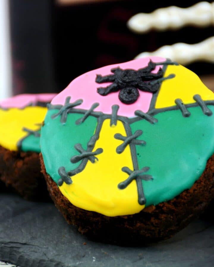 A round brownie decorated with green, yellow, and pink icing with a spider for Halloween.