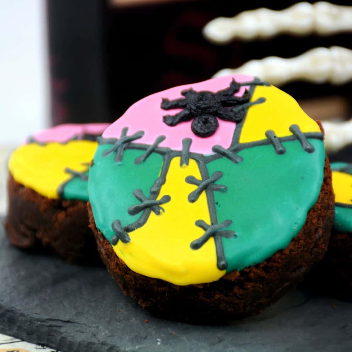 A round brownie decorated with green, yellow, and pink icing with a spider for Halloween.