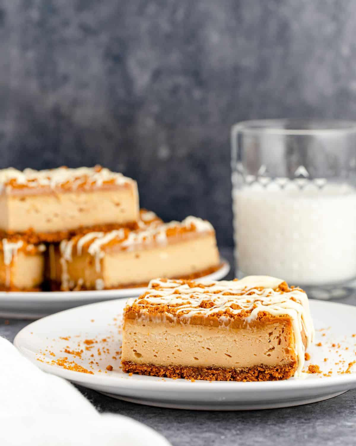 Biscoff cheesecake square on a plate with a drizzle of white frosting.