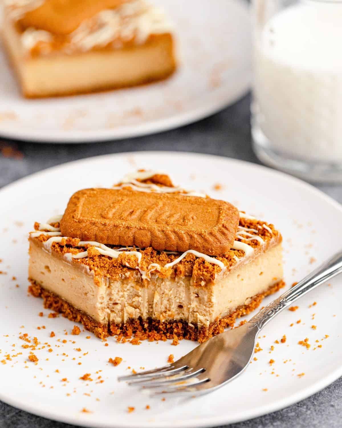 A slice of cookie butter cheesecake bars with a biscoff cookie on top.