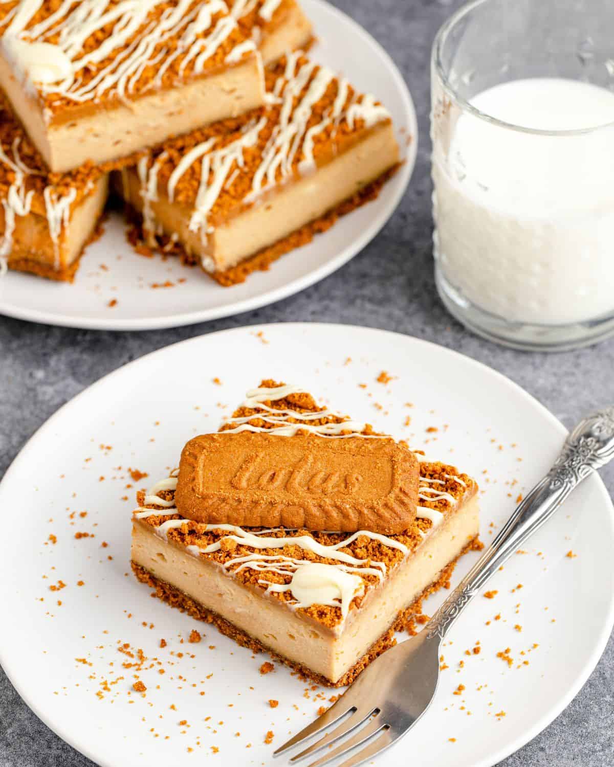 A stack of cookie butter squares on a plate in front of a cheesecake square with a cookie on top of the square.